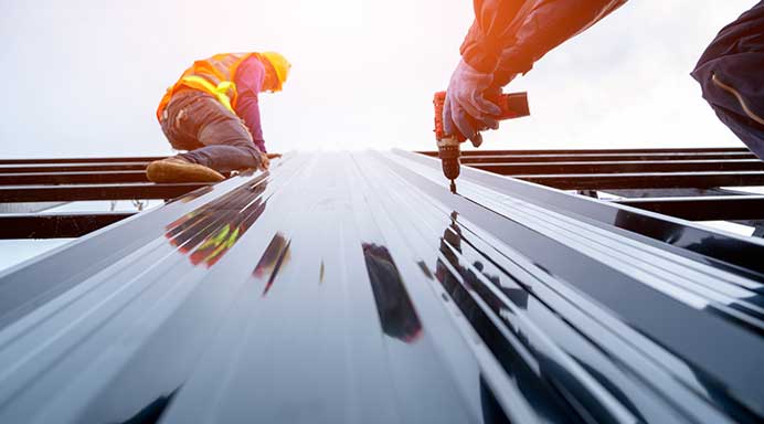 Roofer installing grey long run metal roofing panels on a commercial building in Auckland